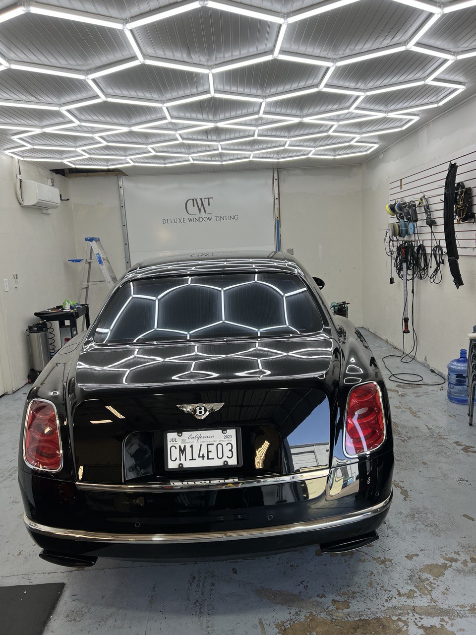 Black Bentley with professional window tinting under hexagonal LED lights in a Gold River shop.