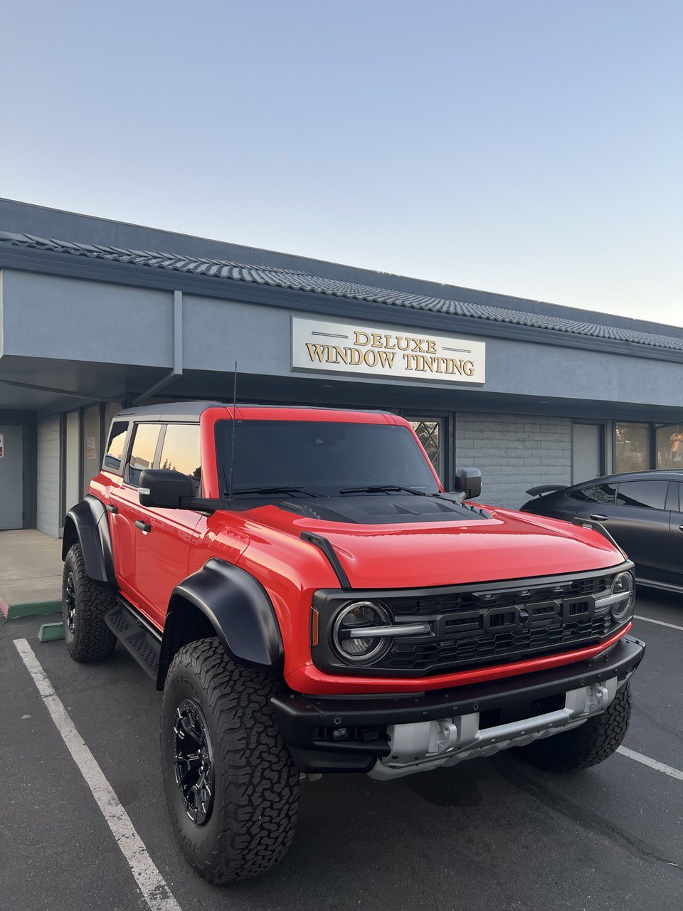 Red Ford Bronco Raptor with dark window tinting parked in front of a tint shop in Gold River, CA.