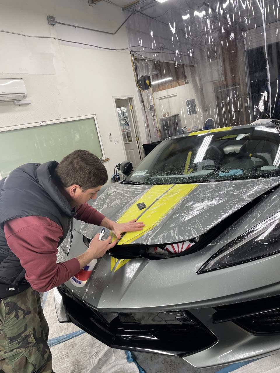 Technician applying paint protection film to a grey sports car with yellow stripes in Gold River, CA.