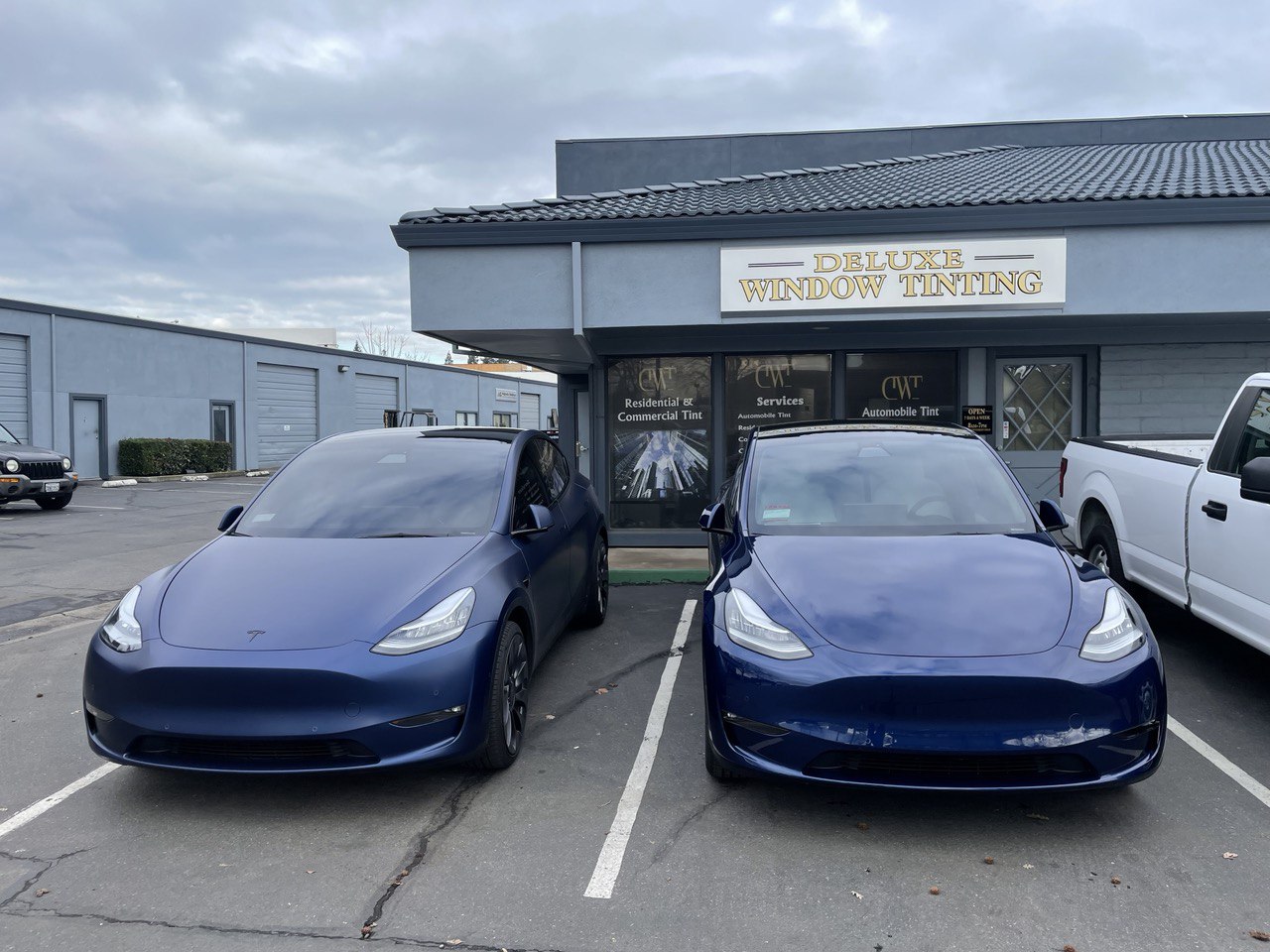 Two blue Tesla Model Y cars with professional window tinting parked in front of Deluxe Window Tinting.